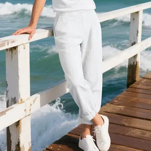 Male model wearing loose white linen trousers standing on a seaside wooden pier