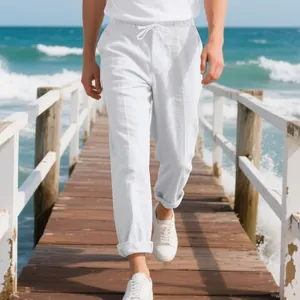 Close-up detail of men's loose white linen beach pants on a sunny ocean pier walkway
