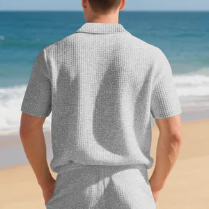 Vue arrière d'un polo gris en maille gaufrée et d'un short sur une plage ensoleillée