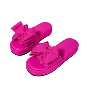 Sandalias de plataforma color magenta con un lazo de tela gigante sobre fondo blanco