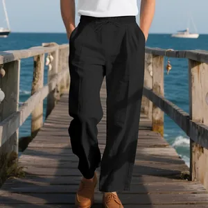Detail view of men's loose black linen casual pants with drawstring waist on a beach