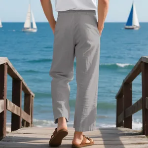 Loose grey linen pants for men styled on a coastal wooden pier with a calm sea view.