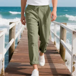 Men's loose sage green linen beach pants with drawstring waist shown on wooden pier