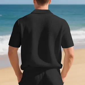 Vue arrière d'un polo noir en maille gaufrée pour homme sur une plage en été.