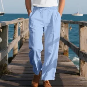 Loose light blue linen trousers for men with drawstring waist in a beach setting.