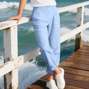 Men's light blue casual linen pants styled with white sneakers on a sunny beach pier