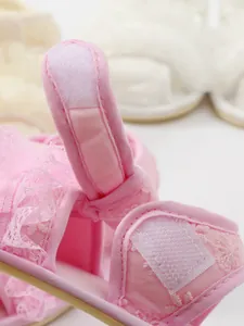 Close-up van roze geborduurd kant en klittenbandsluiting op baby prinsessen sandalen