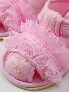 Detailopname van roze babysandalen met delicaat kant en geborduurde bloemdetails.