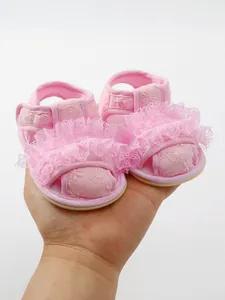 Close-up van roze babysandalen met delicate kanten ruches en bloemige borduurdetails