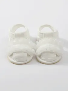 Gedetailleerd aanzicht van witte kanten geborduurde babysandalen met luxe ruches.