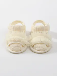 Detailopname van het fijne kant en de geborduurde bloemen op deze baby sandalen.