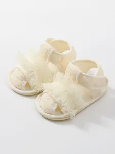 Detail van zachte crème babysandalen met kanten ruches en geborduurde bloempatronen