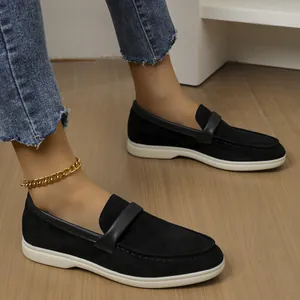 Detail view of black suede-like loafers for women featuring white flat soles on wooden floor