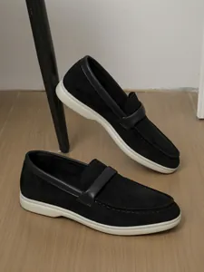Close-up of black suede loafers with contrasting white flat soles in a lifestyle setting.