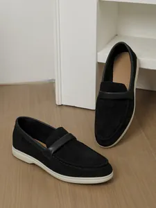 Close-up of black suede loafers on wooden floor with white shelf backdrop