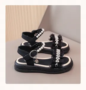 Close-up detail of girls' black princess sandals featuring pearl straps and ruffles.