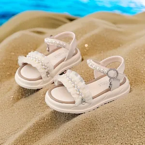 Elegant girls' beige princess sandals with pearls and lace ruffles on beach sand