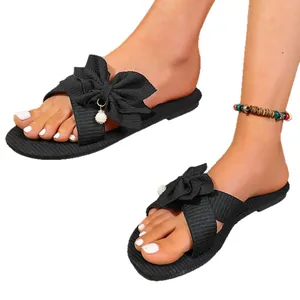 Elegant black flat sandals for women featuring a large ribbed fabric bow and pearl detail.