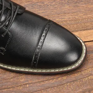 Nahaufnahme des schwarzen Derby-Schuhs aus Leder mit Brogue-Detail auf Holzgrund.