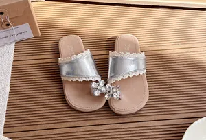 Primer plano detallado de chanclas plateadas para niña con flores de cristal y encaje elegante.