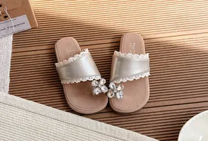 Primer plano de chanclas plateadas para niña con encaje y detalle de flor de strass.