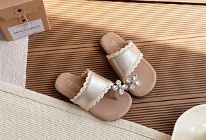 Detalle de sandalias doradas para niña con flor de cristal y ribete de encaje.