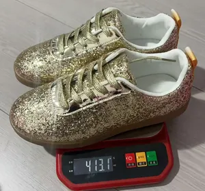 Macro detail of gold glitter flat sneakers showing 413g weight on a red digital scale