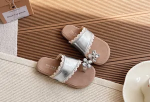 Detalle de sandalias plateadas para niña con flor de pedrería y encaje en suela plana suave.