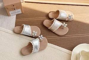 Detalle de sandalias plateadas para niña con encaje y adorno de flor con pedrería