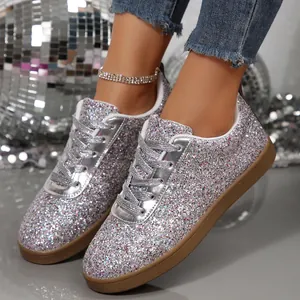 Close-up view of stylish silver glitter flat sneakers with laces on reflective floor
