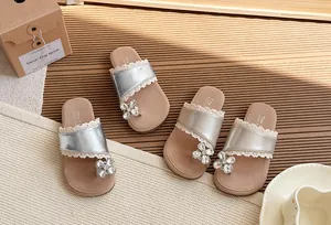 Detalle de sandalias plateadas para niña con flor de cristal y ribete de encaje