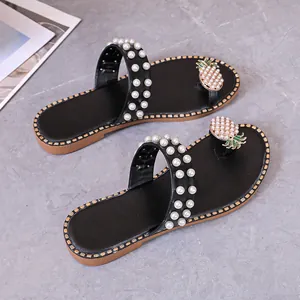 Detailed view of black flat sandals featuring pearl straps and a pineapple toe ornament.