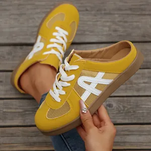 Primo piano di sneakers sabot in mesh giallo da donna con lacci bianchi su legno