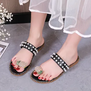Detailed view showing elegant pineapple rhinestone and pearl ornaments on black flat sandals.