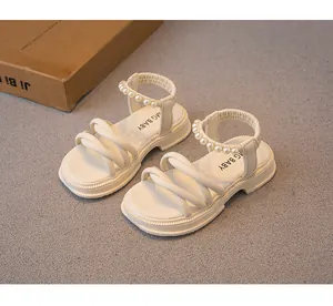 Dettaglio dei sandali da bambina color crema con cinturini di perle e fasce morbide.