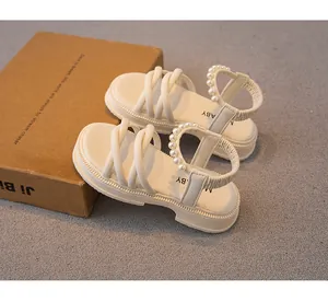 Dettaglio ravvicinato di eleganti sandali panna per bambina con perle e suola piatta.
