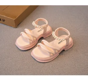 Primo piano di sandali rosa da bambina con cinturini di perle e fasce intrecciate.