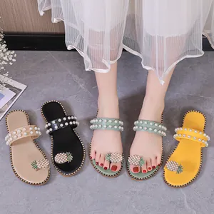 Close-up of flat sandals featuring pearl straps and rhinestone pineapple toe loops