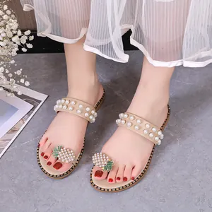Close-up detail of beige summer flat sandals with pearl straps and pineapple rhinestone