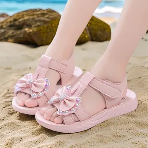 Sandalias de princesa rosas para niña con lazo de diamantes en la arena.
