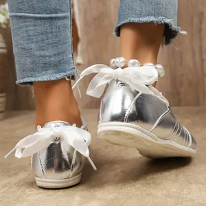 Gros plan de chaussures plates argentées avec nœud en ruban blanc et bracelet de perles