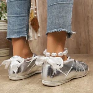 Détail de baskets argentées pour femmes avec d'élégants nœuds en ruban blanc et des perles.