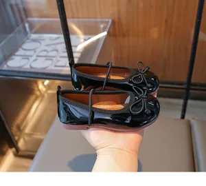 Close-up of shiny black girl's Mary Jane shoes with elegant bow detail held by hand.