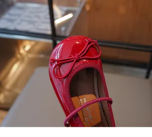 Macro view of the shiny red patent leather and delicate bow detail on toddler girl shoes.