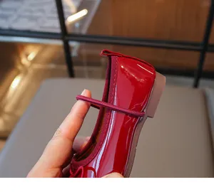 Close-up of glossy red girl shoes with flexible elastic strap and cute bow detail.