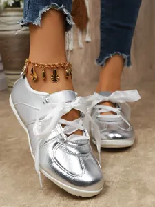 Detailed close-up of metallic silver German trainer sneakers with white ribbon laces