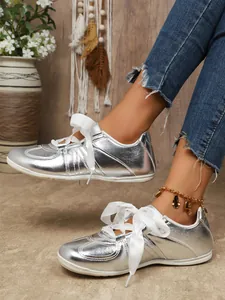 Close-up of shiny silver metallic trainer sneakers featuring elegant white ribbon laces