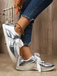 Close-up detail view of trendy silver metallic sneakers with stylish white ribbon laces on model