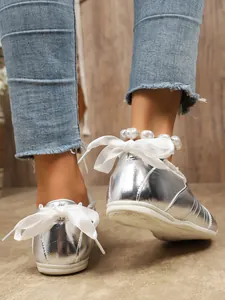 Detailed view of silver metallic sneakers featuring a white bow and pearl anklet