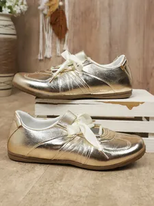 Detail view of gold metallic retro sneakers with elegant white satin ribbon laces